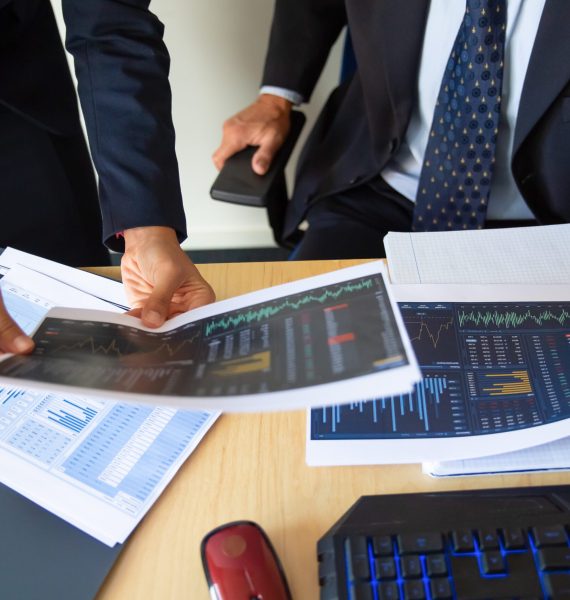 Investor and trader discussing statistic data, holding papers with financial charts and pen. Cropped shot. Broker job or trading concept